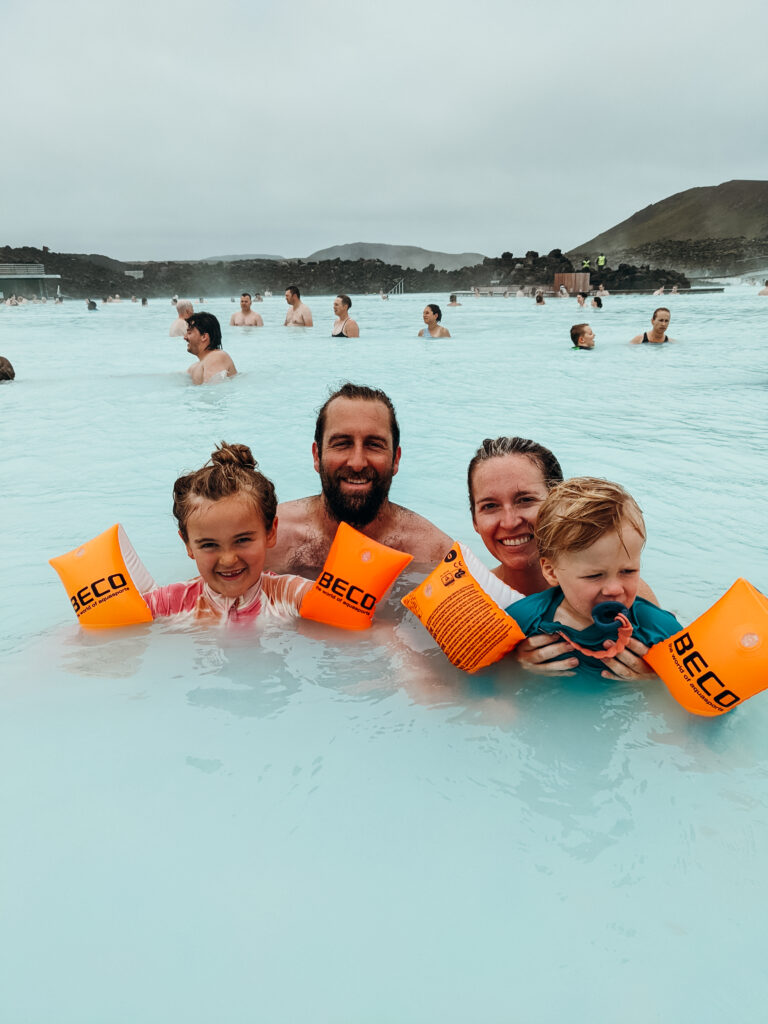 A family smiles with two young children in the silica waters of the Blue Lagoon, one of the best kid-friendly Icelandic geothermal pools.