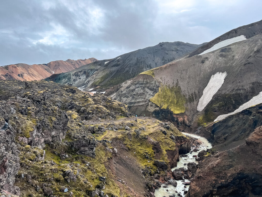 Black volcanic rocks covered in snow frame the painted mountains of Landmannalaugar.