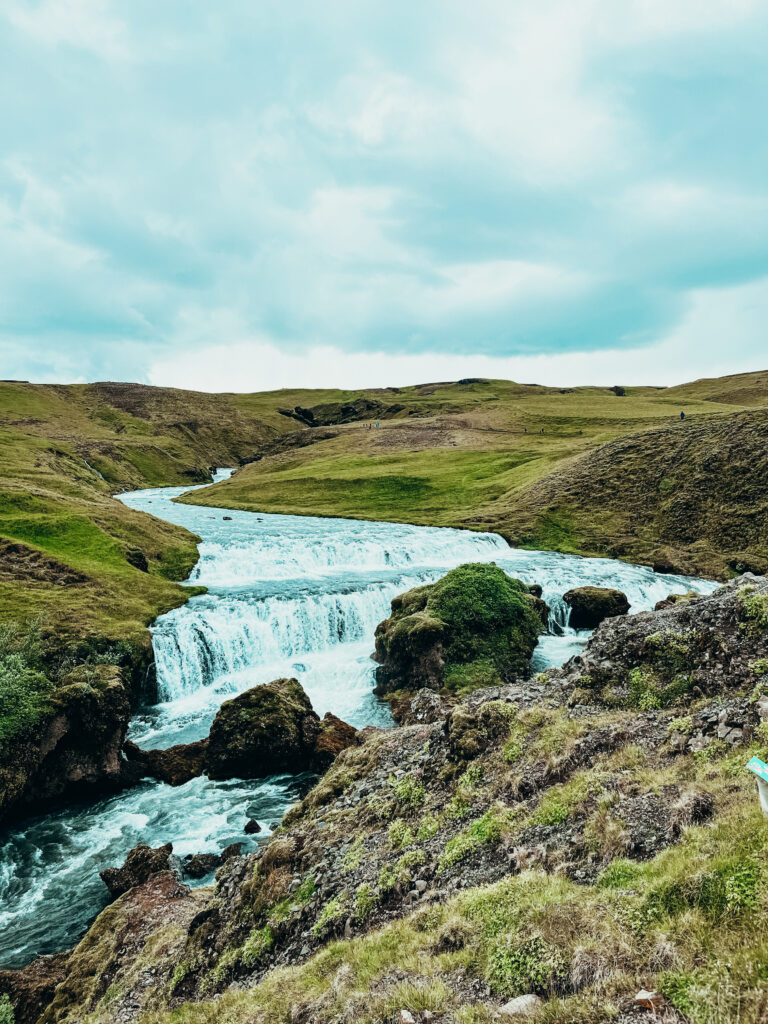 The Skogafoss waterfall flows between two grassy river banks.