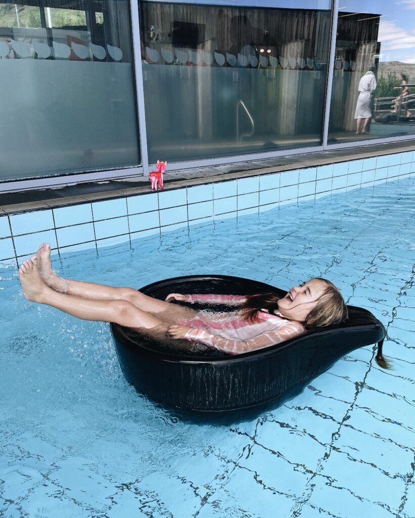 A young girl sits in a water sculpture laughing in a geothermic hot spring.