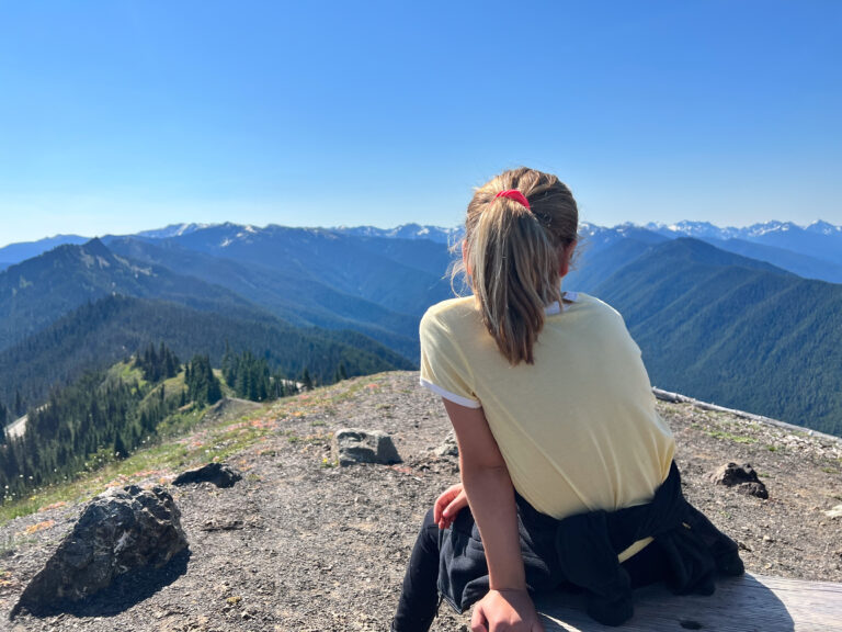 A young girl in a yellow shirt looks out at Hurricane Ridge in Olympic National Park.