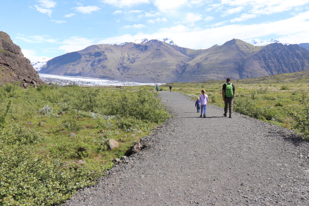 A dad walks with his two young children  on a gravel trail towards the tongue of a glacier.