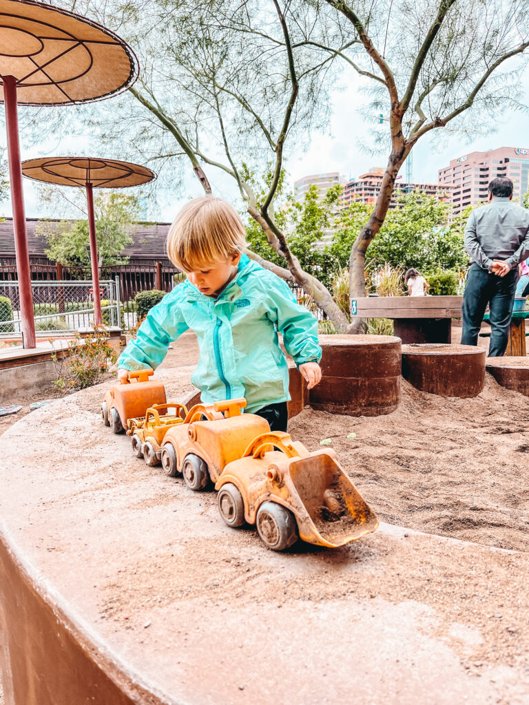 A young boy pulling a chain of construction play toys on a dirty wall at the Children's Museum of Phoenix, one of the best Scottsdale activities for kids.