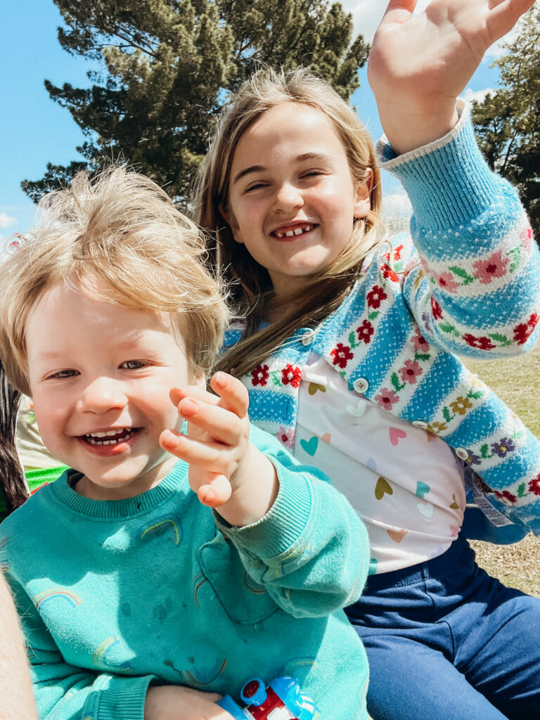 Two children riding on a mini chain and waving for the camera.