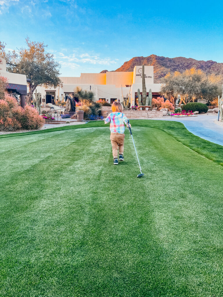 A toddler boy pulling a golf club in front of the best resorts in Scottsdale for families, the JW Marriott Camelback Inn.