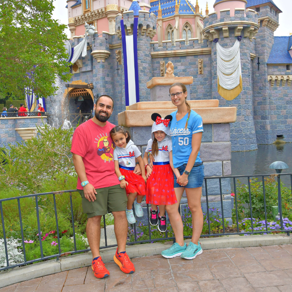 The Disneyland expert, Katie smiles with her husband and two daughters in front of Cinderella's castle.